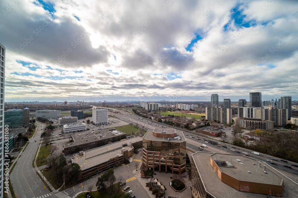 Fototapeta premium Expansive view over a vibrant urban landscape featuring high rise buildings, busy highways with moving traffic, and a large city skyline stretching towards the horizon under a cloudy sky
