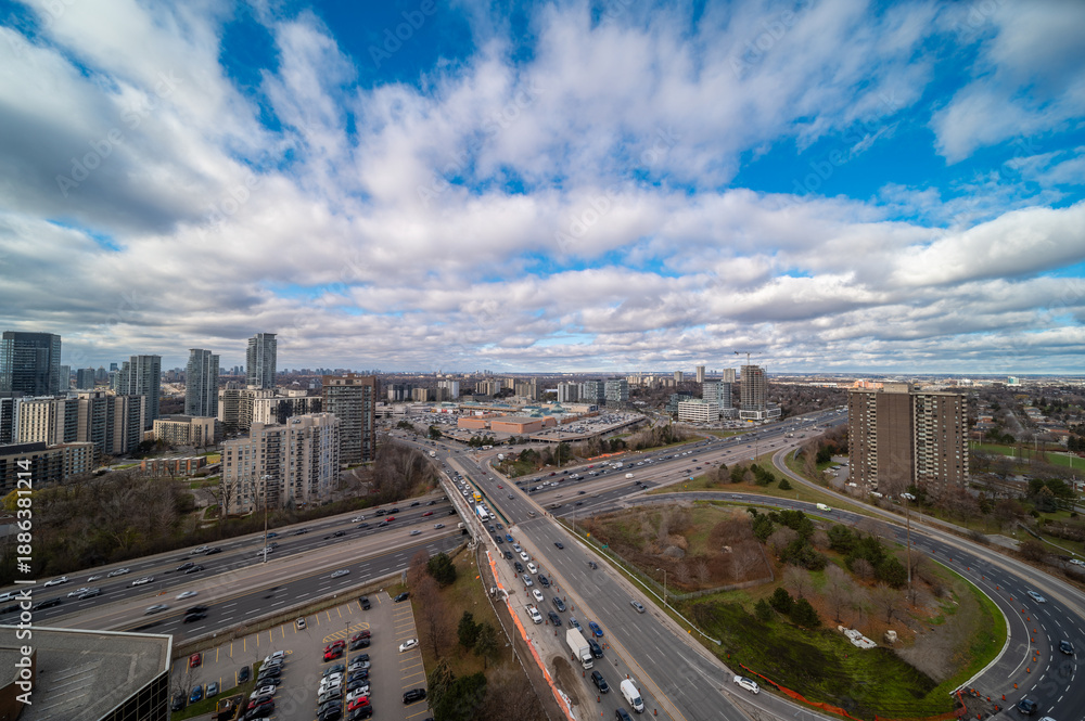 Fototapeta premium Cityscape showcasing a sprawling highway network with heavy vehicle traffic during the day, surrounded by commercial and residential high rise buildings under a cloudy blue sky