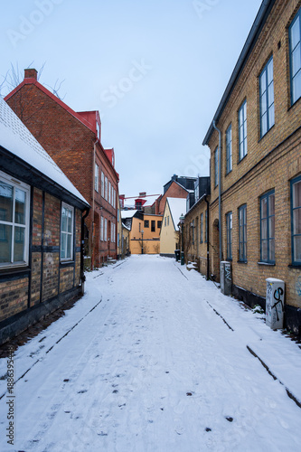 Empty narrow cobblestone street covered in snow between historic brick buildings in winter in Lund Sweden