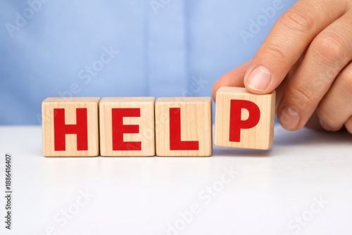 Solicitous Proposition: A hand carefully positions a wooden block, assembling the word HELP, in a poignant depiction of assistance and empathy.