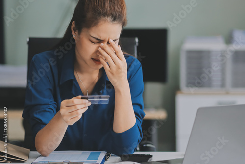 Young businesswoman is holding two credit cards with a worried expression, trying to decide which one to use to pay off her debt