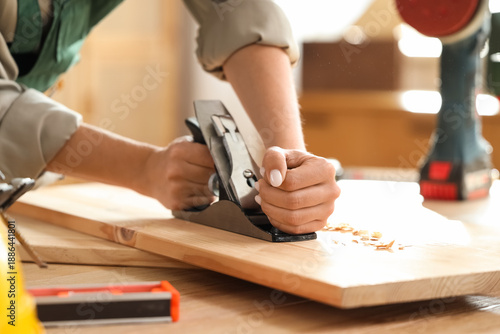 Fotografie Young female carpenter planing wooden plank with hand plane in workshop, closeup