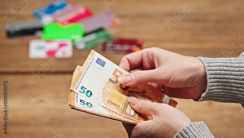 Woman counting euro banknotes with various credit cards in the background on a table, illustrating finance, payment, personal savings, and money management concepts.