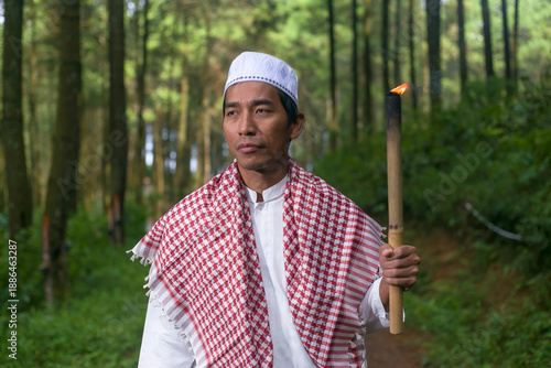 Photos An Asian Indonesian man stands holding a torch wearing Muslim attire, a peci and
