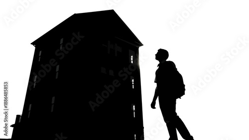 Silhouette of a person with a backpack looking up at a tall building.