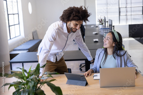 Diverse coworkers in business attire discussing project on laptop and tablet at office