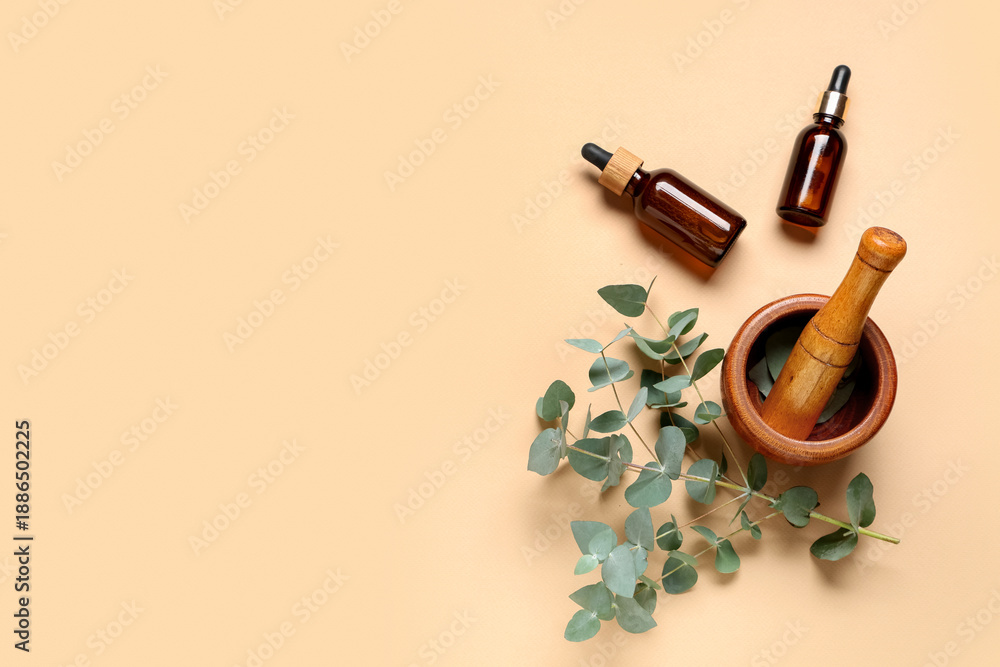 Obraz premium Wooden mortar and pestle with eucalyptus branch and bottles of essential oil on beige background