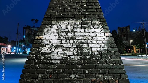 A dark brick structure dominates, contrasting against a night scene with streetlights and buildings