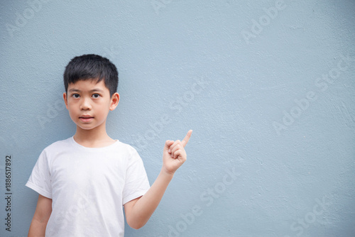 An Asian boy wearing a white shirt is pointing to the side in the blank space for text.