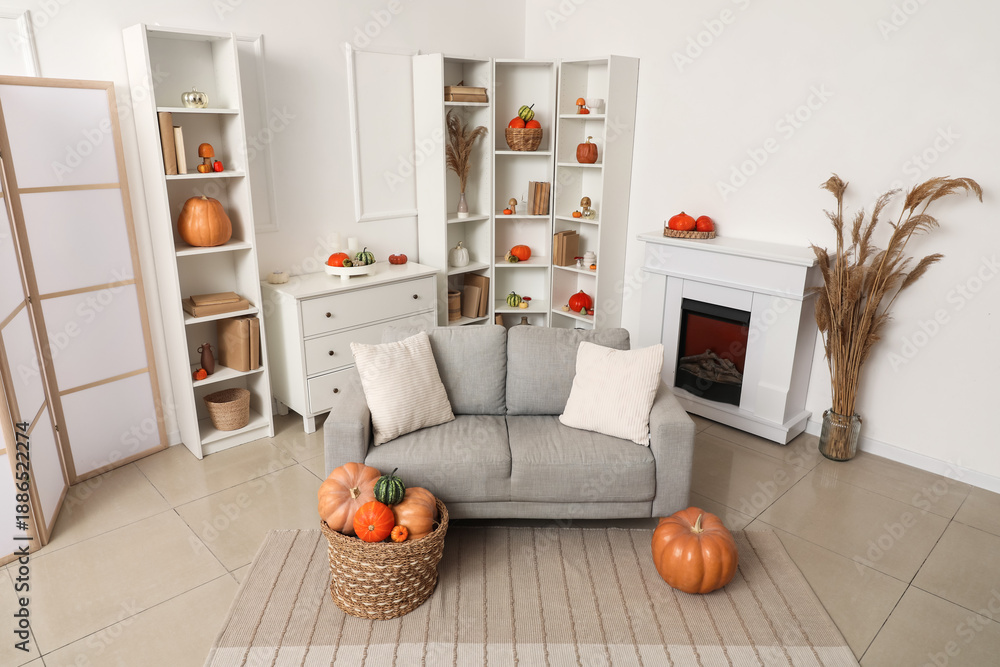 Fototapeta premium Living room interior with grey sofa, shelving units, fireplace and wicker baskets of different pumpkins
