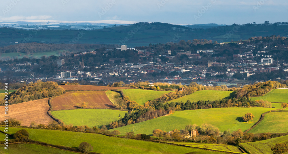 Naklejka premium Long distance telephoto shot of Exmoor National Park from the outskirts of Dartmoor National Park with the city of Exeter in between showing two seasons in one day.