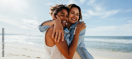 Photos Two friends hugging and smiling together at the beach on a sunny day