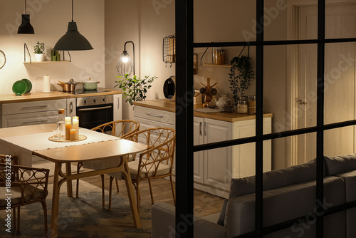 Foto Interior of modern kitchen with glowing lamps, white counters, sofa and dining t