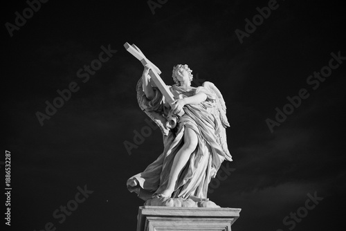 Fotografia The angel with the cross on Ponte Sant’Angelo stands in quiet grace, watching over Rome’s timeless history and flowing river