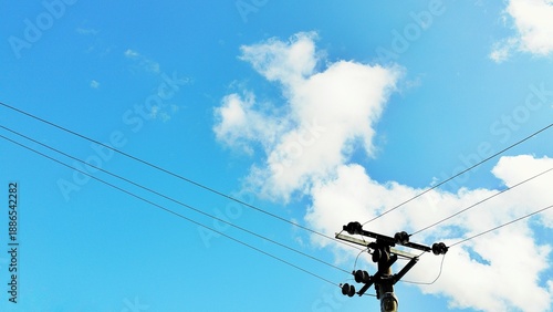Low angle view of metal lattice electricity tower and power cables under a sunny blue sky.