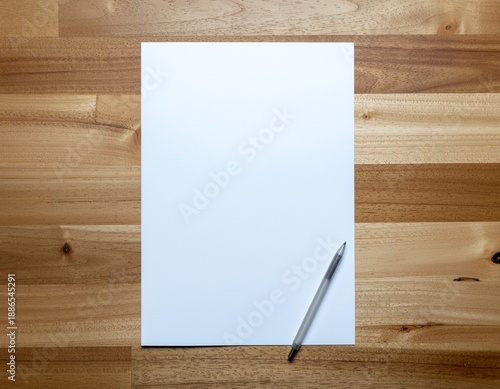 A blank white sheet of paper with a pen lies on a wooden surface viewed from directly above in a minimalist setting