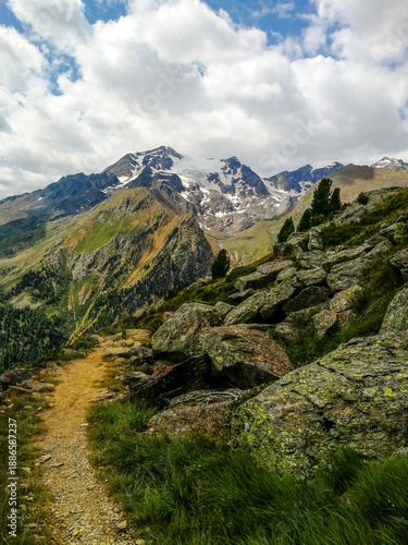 Vertical View of a Narrow Alpine Trail Along a Rocky Ridge with Snowy Peaks, Dramatic Clouds and Tree Line in the High Mountains of Valle Camonica, Italy