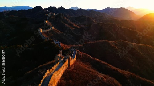 Aerial view of the majestic Great Wall snaking through the rugged, mountainous terrain, bathed in the warm glow of the setting sun, Huairou District, China.