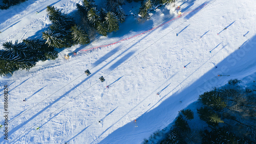 Top down aerial view of skiers moving across groomed snow slope, creating dynamic patterns and long shadows, suitable for winter sports and outdoor concepts
