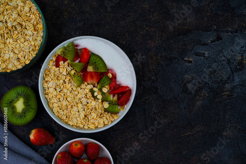 Healthy morning oatmeal bowl richly topped with sliced kiwi and fresh strawberries, presented alongside raw oats for a nutritious breakfast concept.