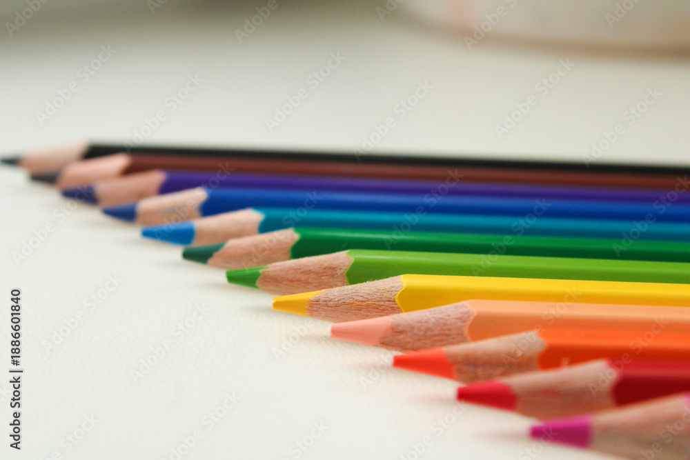 Obraz premium Row of sharpened colored pencils arranged diagonally showing rainbow gradient spectrum with detailed wooden tips visible on neutral background.