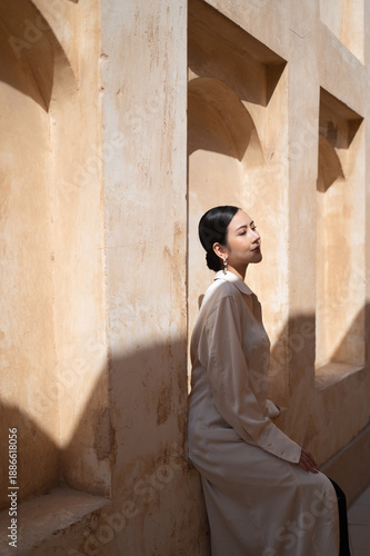 A beautiful woman in a light beige abaya poses in profile in soft natural light.