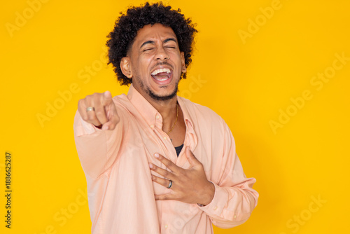 young latino man with afro hair isolated on white background pointing and laughing out loud