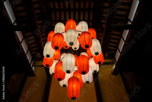 Cluster of red and white paper lanterns hanging from traditional wooden ceiling, creating warm ambient lighting in Asian interior architecture.