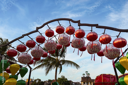 Red Chinese lanterns hanging on decorative arch against blue sky with palm tree