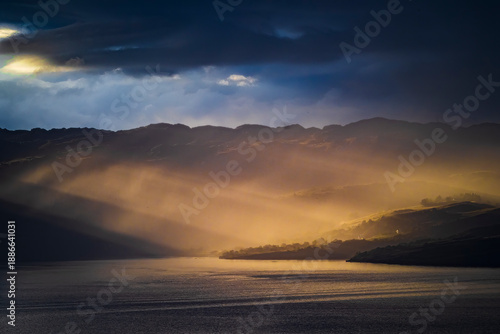 Sunbeams breaking through clouds over Scottish loch