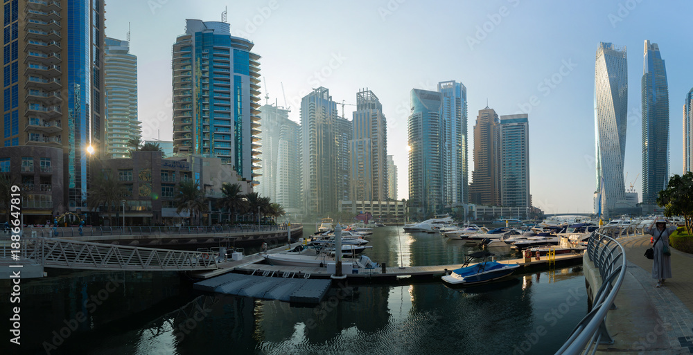 Fototapeta premium Evening view of a river canal and a ship. Orange sunlight, skyscrapers, buildings and the embankment. On the streets of the Emirates, in a public place.