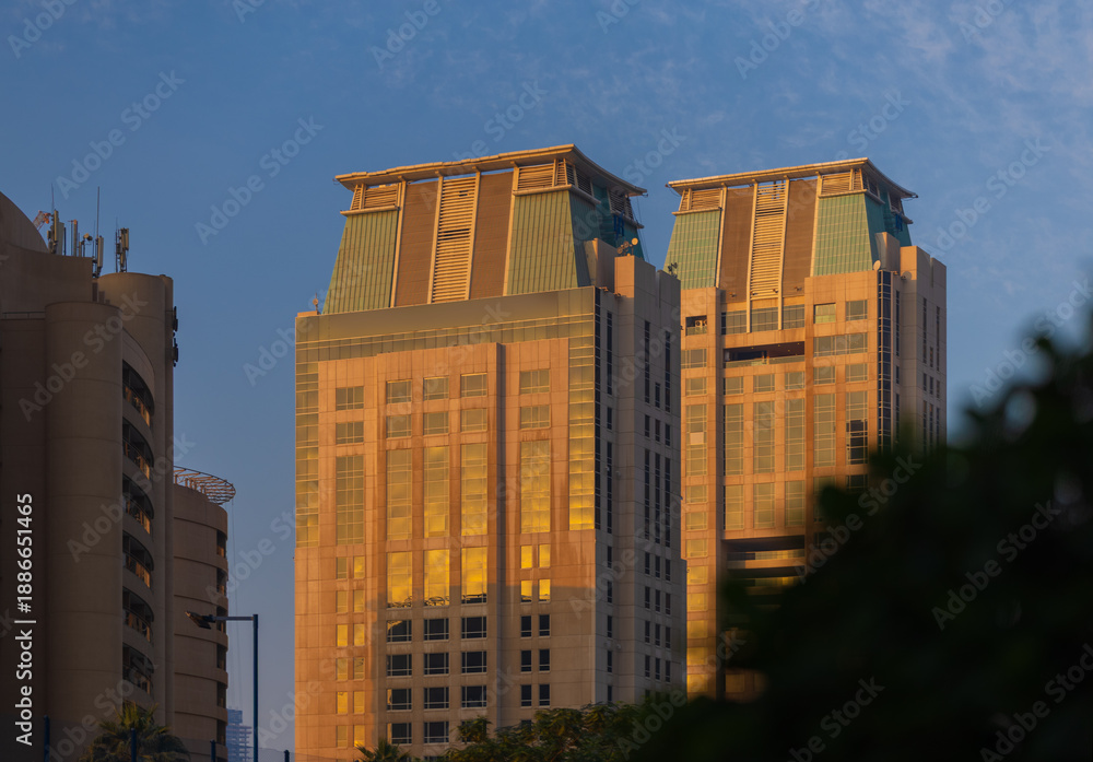 Obraz premium Evening view of the city. Orange sunlight, skyscrapers, buildings, and city streets. On the streets of the Emirates, in a public space.