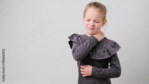 Young child girl touches throat frowning with a sad face, showing signs of pain and discomfort related to sore throat or illness. School kid isolated on white background.