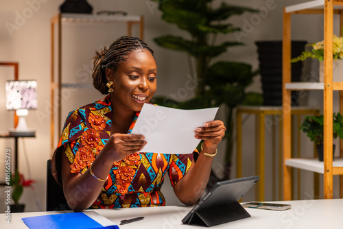 Canvas Print Smiling young African woman holding letter, doing paperwork, reading good news a