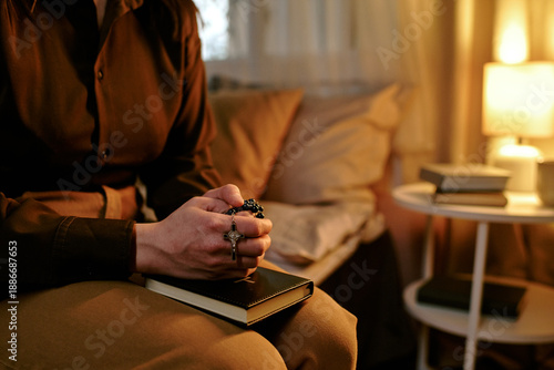 Obraz na plátně Woman sitting on sofa holding rosary and closed book with both hands, clasping f