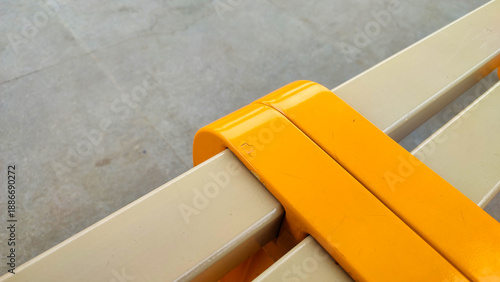 Close-up view of a modern yellow and tan slatted bench at a train station, highlighting the smooth surface texture. Suitable for public transport, urban design, travel concepts and abstract background