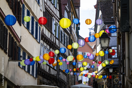 View of vibrant lanterns strung across a narrow street framed by half-timbered buildings, casting colorful glows in Tubingen, Baden-Wurttemberg, Germany.
