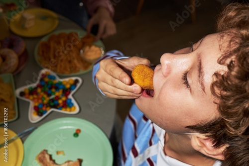 Foto Caucasian boy eating chicken nugget at table, tilting head back with mouth open,
