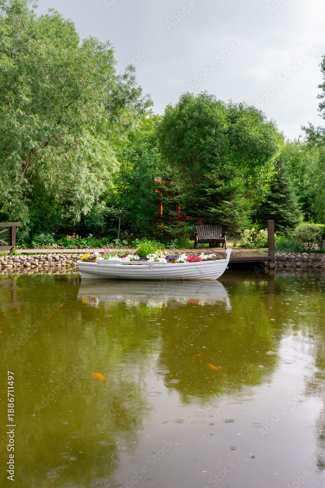 Fototapeta premium Rain in the summer park. A pond with a boat under raindrops.