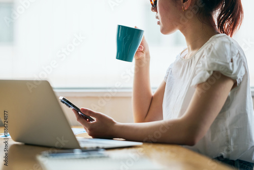 Young Asian woman working remotely on a laptop while drinking coffee at home