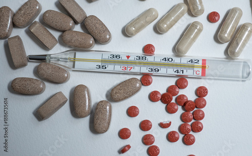 Medical thermometer with pills on white background