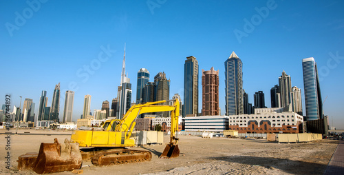 Bulldozer on the sand against the backdrop of skyscrapers in Dubai as a symbol of UAE development