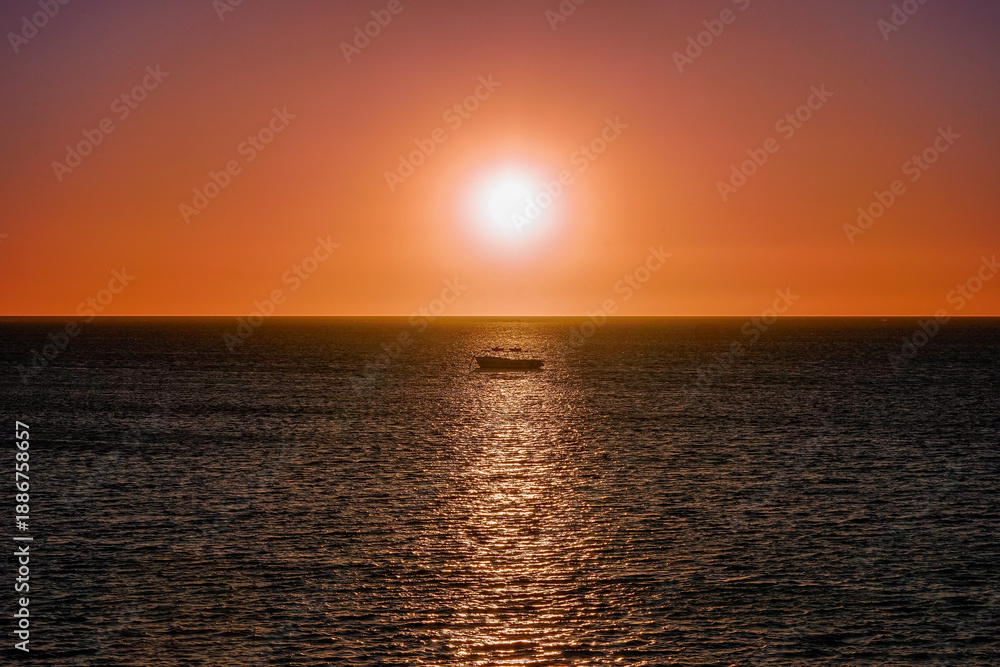 Obraz premium Red Sunset over ocean horizon with a boat in sunlight