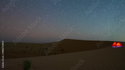 Timelapse of the night sky camping with glowing tent , the slider motion in the desert sand dune.