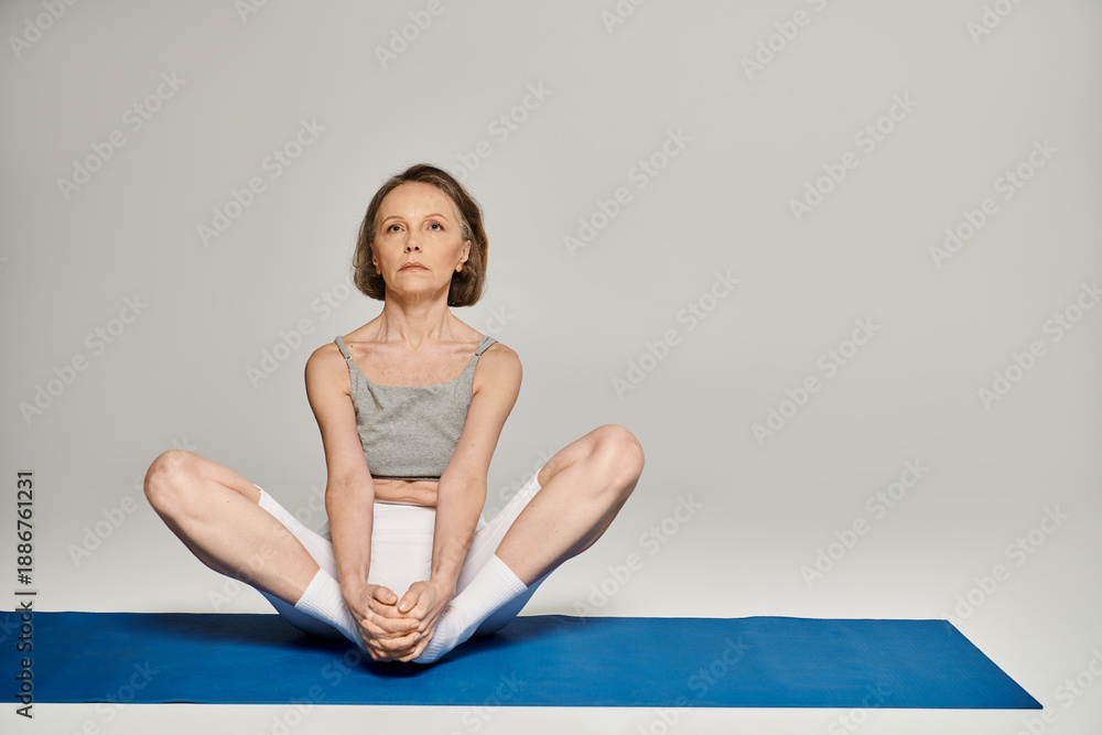 Fototapeta premium Mature woman practicing yoga poses gracefully on a blue mat in a tranquil studio