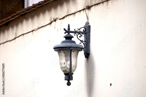 Vintage wall lantern with ornate metal bracket mounted on light facade, elegant architectural detail with classic outdoor lighting atmosphere.
