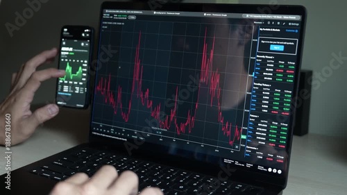 close up smartphone with laptop and open stock exchange, trading Online app interface. Man hand scrolling touch screen analysing chart forex crypto currency.