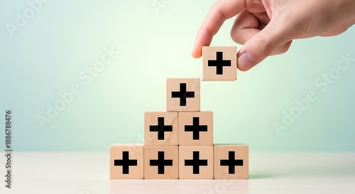 Human hand stacking wooden blocks with black plus symbols representing business growth, addition, and positive progress