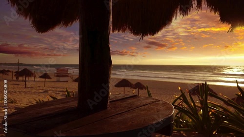 Cinematic Golden Hour View of a Tropical Beach through a Traditional Thatched Palapa. traditional thatched palapa. The golden sun dips toward the horizon, travel agencies, hospitality marketing conce 