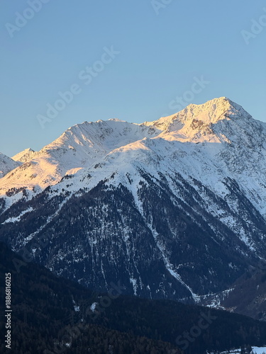 Snow-covered alpine mountain range at sunrise with golden light on peaks, clear blue sky, winter landscape, nature background, wilderness, travel destination, serene outdoor scenery, Switzerland 